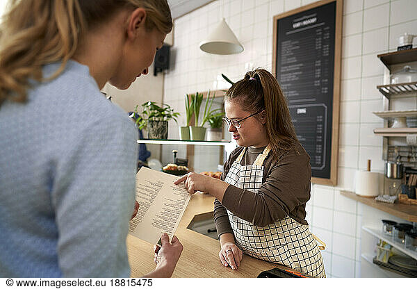 Cafe owner with down syndrome helping customer to choose food from menu in coffee shop