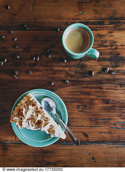 Cake slice and coffee with scattered roasted beans on table