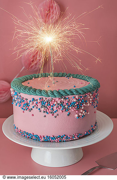 Cake stand with strawberry birthday cake decorated with burning sparkler