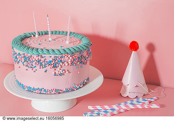 Cake stand with strawberry birthday cake  drinking straws and party hats