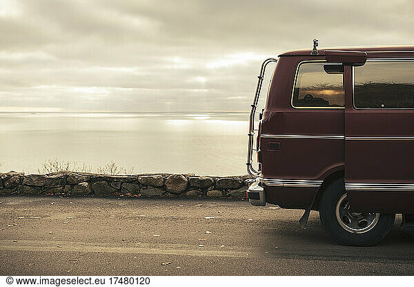 Camper van on roadside near sea against cloudy sky