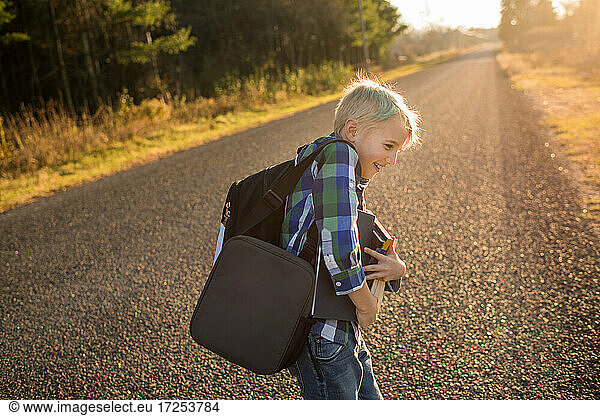 Canada  Ontario  Smiling boy with books on rural road at sunset