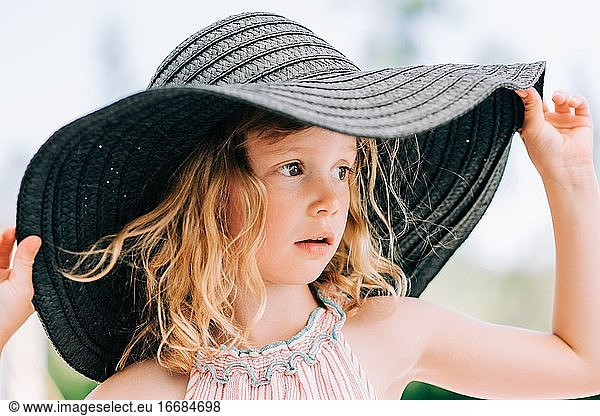 candid close up portrait of a young girl stood outside with a sun hat