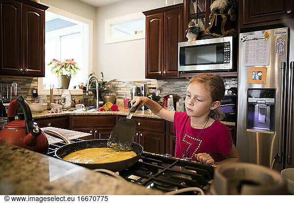 Candid Image of Unsmiling Young Girl Cooking Eggs In Messy Kitchen