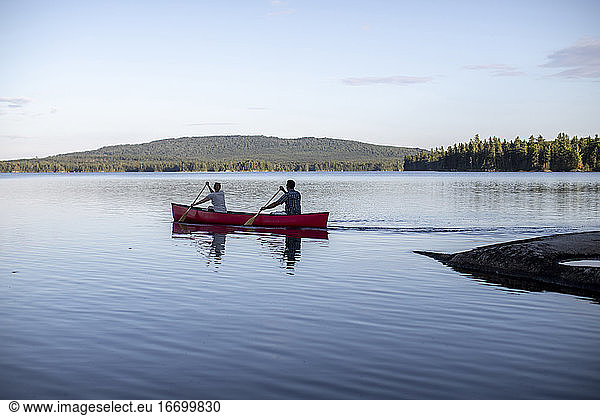 Canoe paddled by two people heads into the distance on lake in Maine