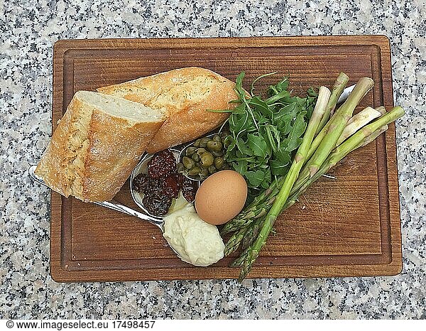 Capers  dried tomatoes  egg  mayonnaise Rocket and green asparagus on dark wooden board  top view  from above