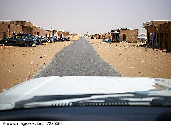 Car driving along asphalt road cutting through remote sandy town
