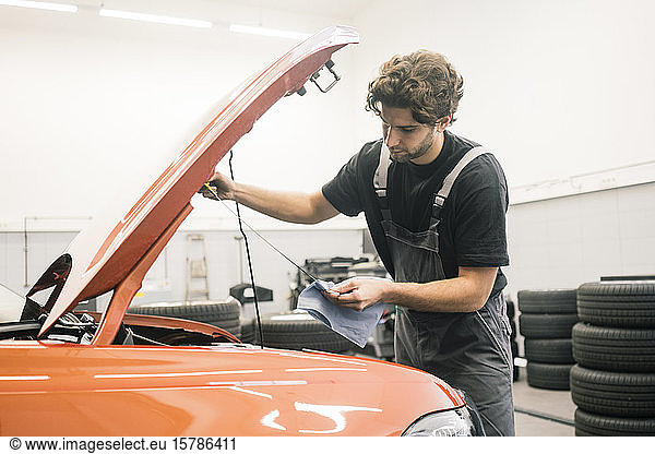 Car mechanic in a workshop working at car checking dipstick