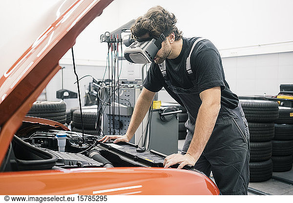Car mechanic wearing VR glasses in a workshop working at car