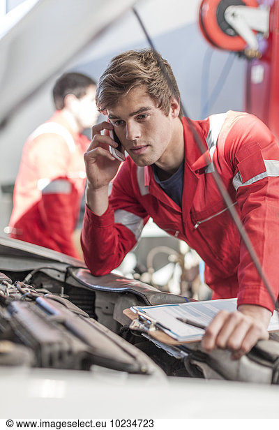 Car mechanic with mobile phone in repair garage