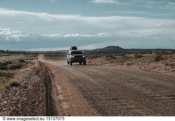 Car on dirt road against cloudy sky