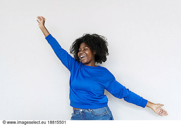 Carefree Afro woman with arms outstretched standing against white background