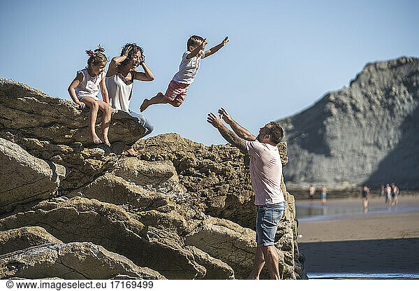 Carefree boy jumping onto father while mother and sister watching at beach