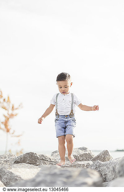 Carefree boy walking on stones against clear sky