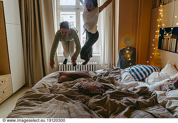 Carefree female friends jumping on bed at home