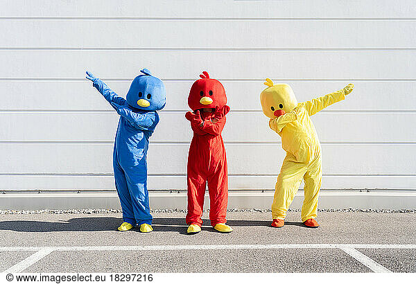 Carefree friends wearing multi colored duck costumes standing in front of wall