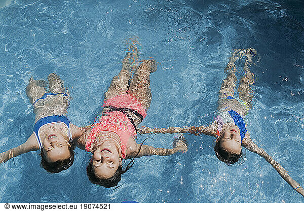 Carefree friends with arms outstretched swimming in pool