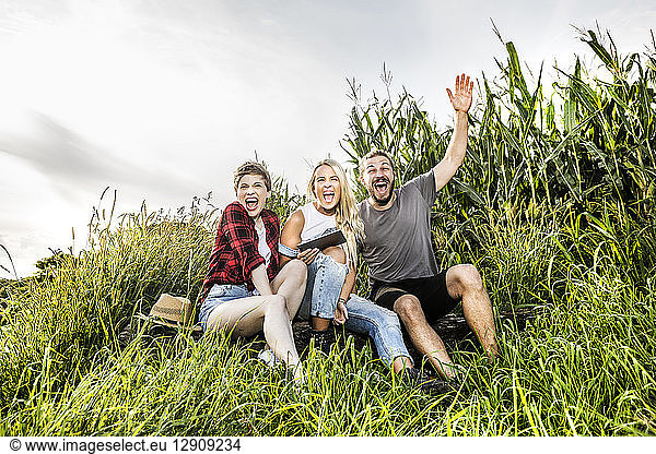 Carefree friends with tablet sitting at a cornfield