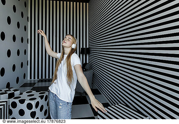 Carefree girl listening music through headphones dancing by striped wall