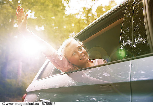 Carefree girl reaching arm out sunny car window