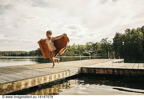 Carefree girl running on jetty while holding towel during vacation