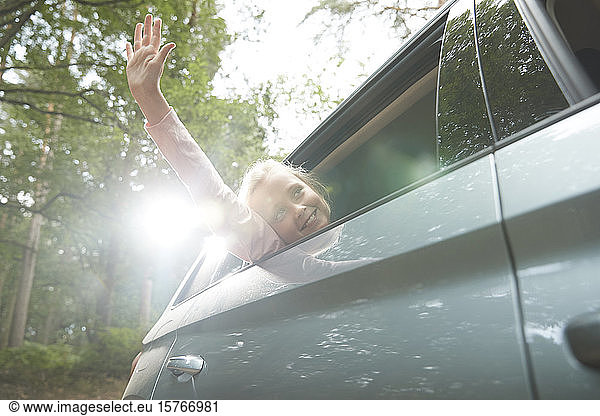 Carefree girl with arm out sunny car window