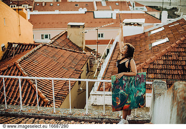 Carefree happy woman with painting on tiled rooftop in Lisbon