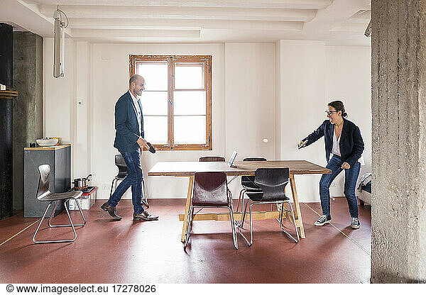 Carefree man and woman playing table tennis while standing at office