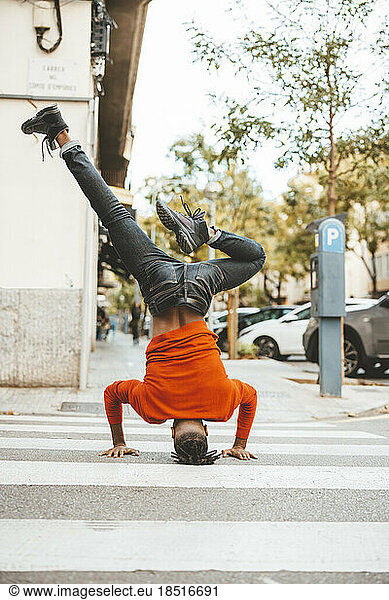 Carefree man doing headstand on zebra crossing at road
