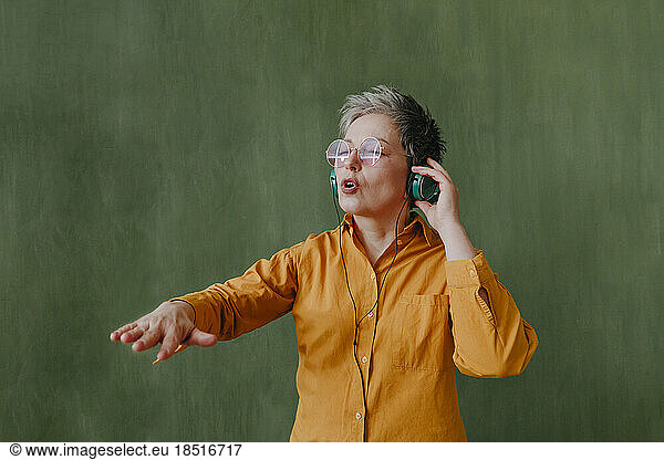 Carefree mature woman enjoying music through wireless headphones in front of green wall