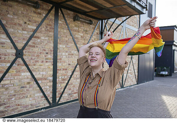 Carefree non-binary person holding LGBTQIA pride flag on street