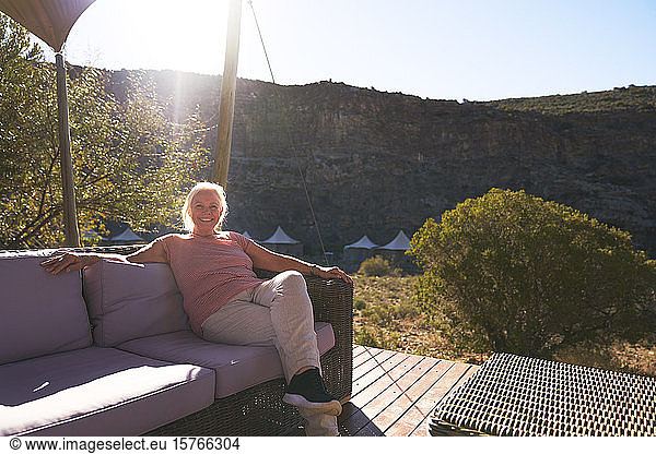 Carefree senior woman relaxing on sunny safari lodge balcony
