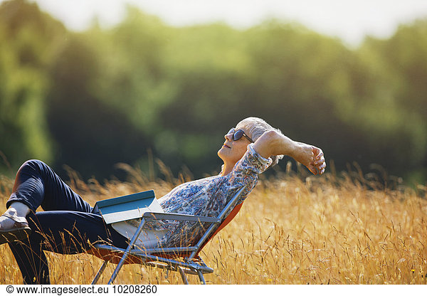 Carefree senior woman relaxing with book in sunny field