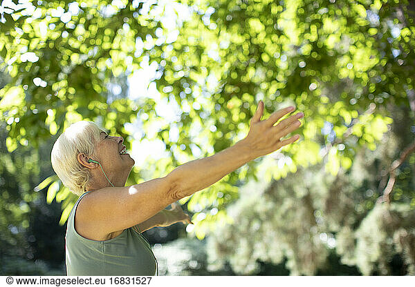 Carefree senior woman with arms outstretched under summer trees