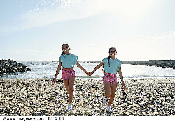 Carefree twin sisters holding hands and walking at beach