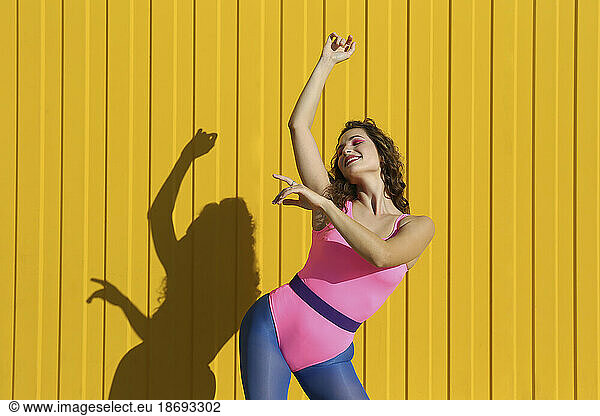 Carefree woman dancing in front of yellow wall