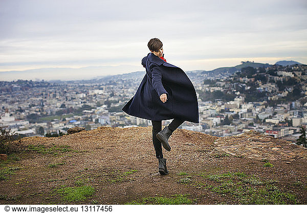 Carefree woman dancing on mountain top with cityscape in background