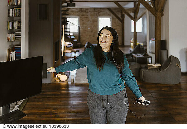 Carefree woman dancing while listening to music in living room at home