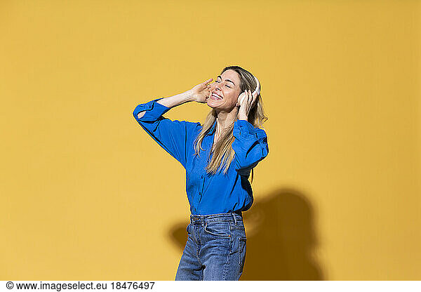 Carefree woman enjoying listening to music against yellow background