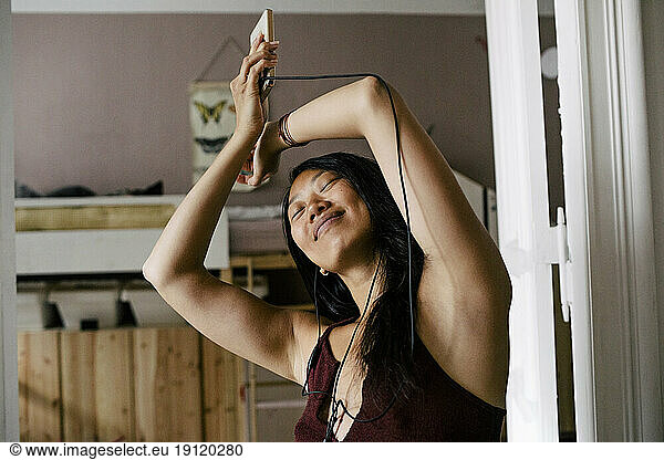 Carefree woman enjoying music through earphones at home
