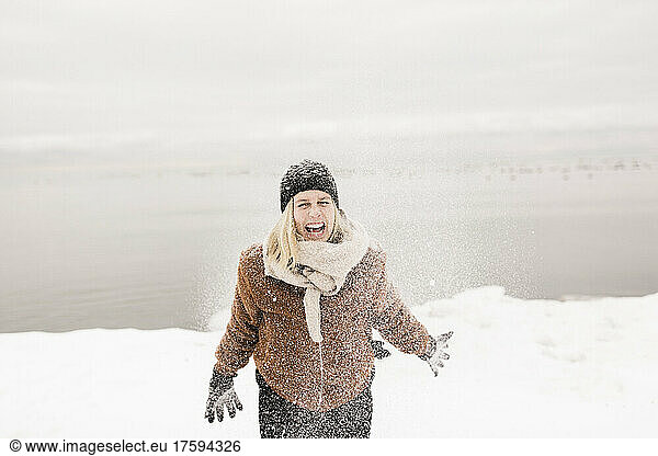 Carefree woman in warm clothing playing with snow in winter