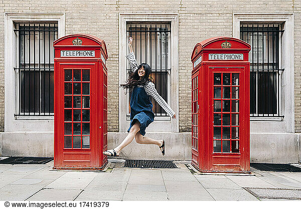 Carefree woman jumping in front of telephone booth