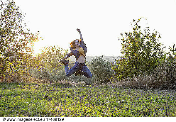 Carefree woman jumping over grass at sunset