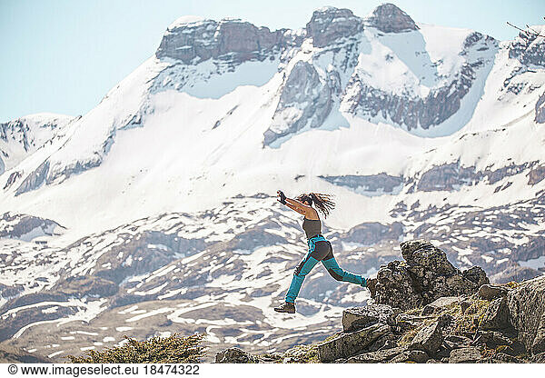 Carefree woman jumping over rocks in front of mountains