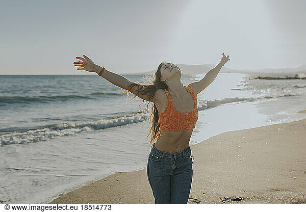 Carefree woman standing at beach with arms raised