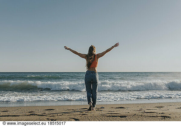 Carefree woman standing with arms outstretched in front of sea