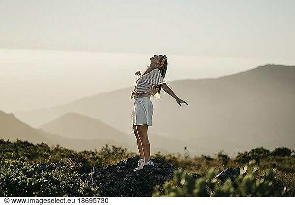 Carefree woman standing with arms outstretched on mountain