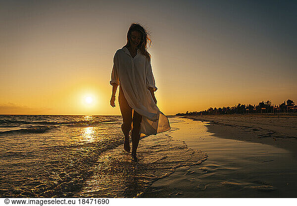 Carefree woman strolling near shore on beach at sunrise