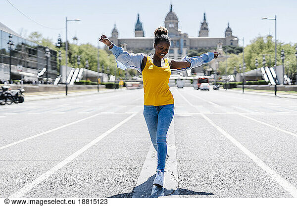 Carefree woman walking with arms outstretched on road at sunny day