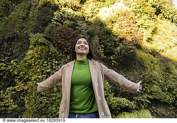 Carefree woman with arms outstretched outside vertical garden
